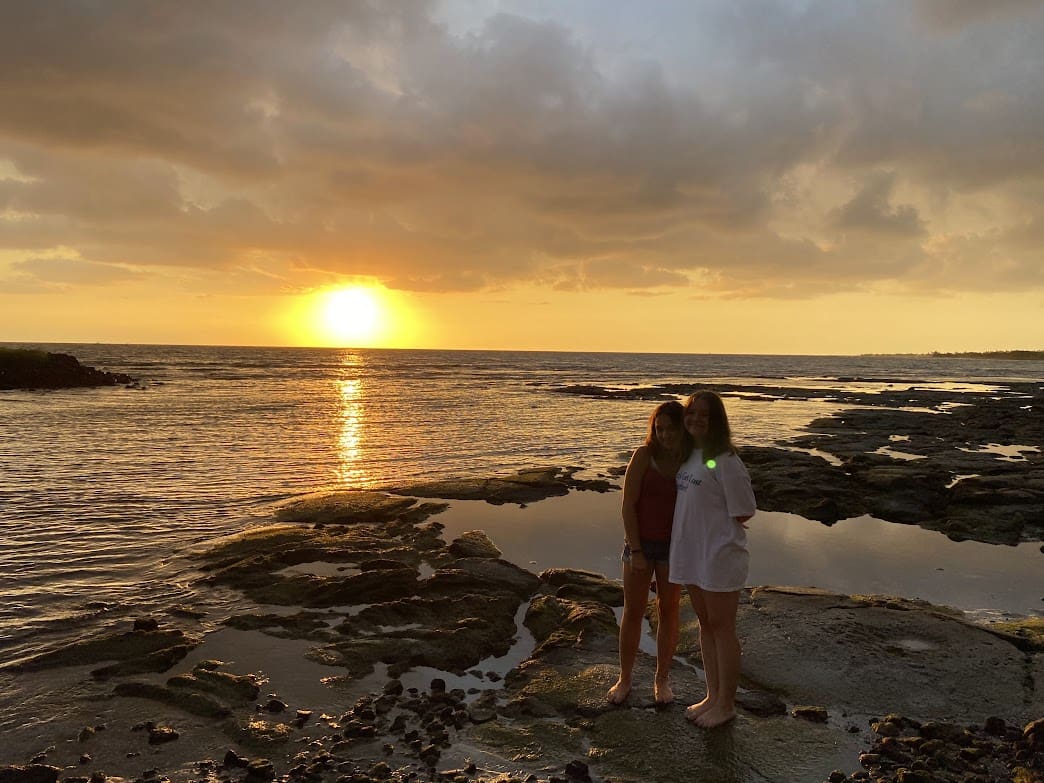 Two women standing on the beach at sunset.