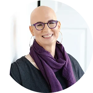 A woman with glasses and bald head wearing a purple scarf.