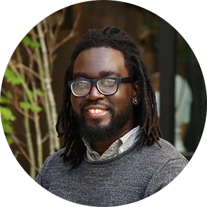 A man with dreads and glasses is smiling.