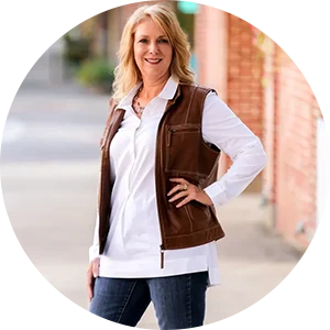 A woman standing on the sidewalk wearing jeans and a brown vest.